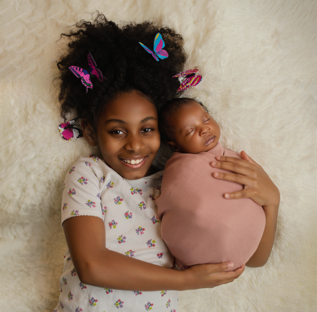 Baby girl and her older sibling laying on a faux blanket for a newborn photography prop.