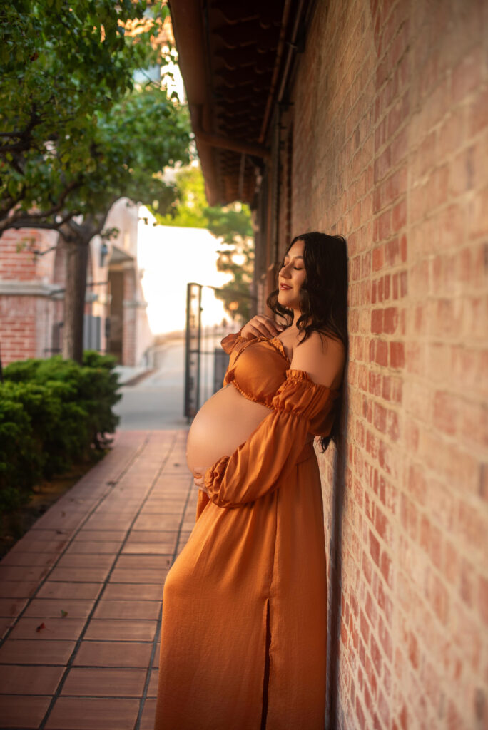 Expecting mom leaned against the brick wall for maternity session at Malaga Cove Plaza in Palo Verde in California