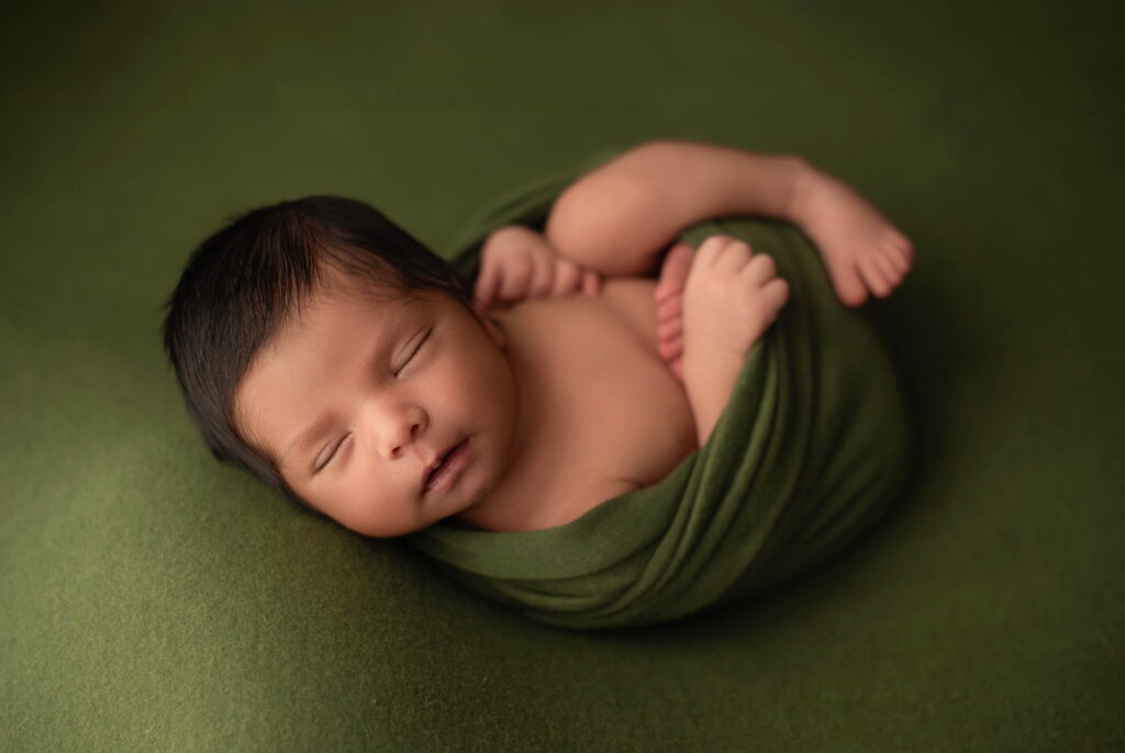 Baby wrapped in green fabric on a green fabric sleeping.