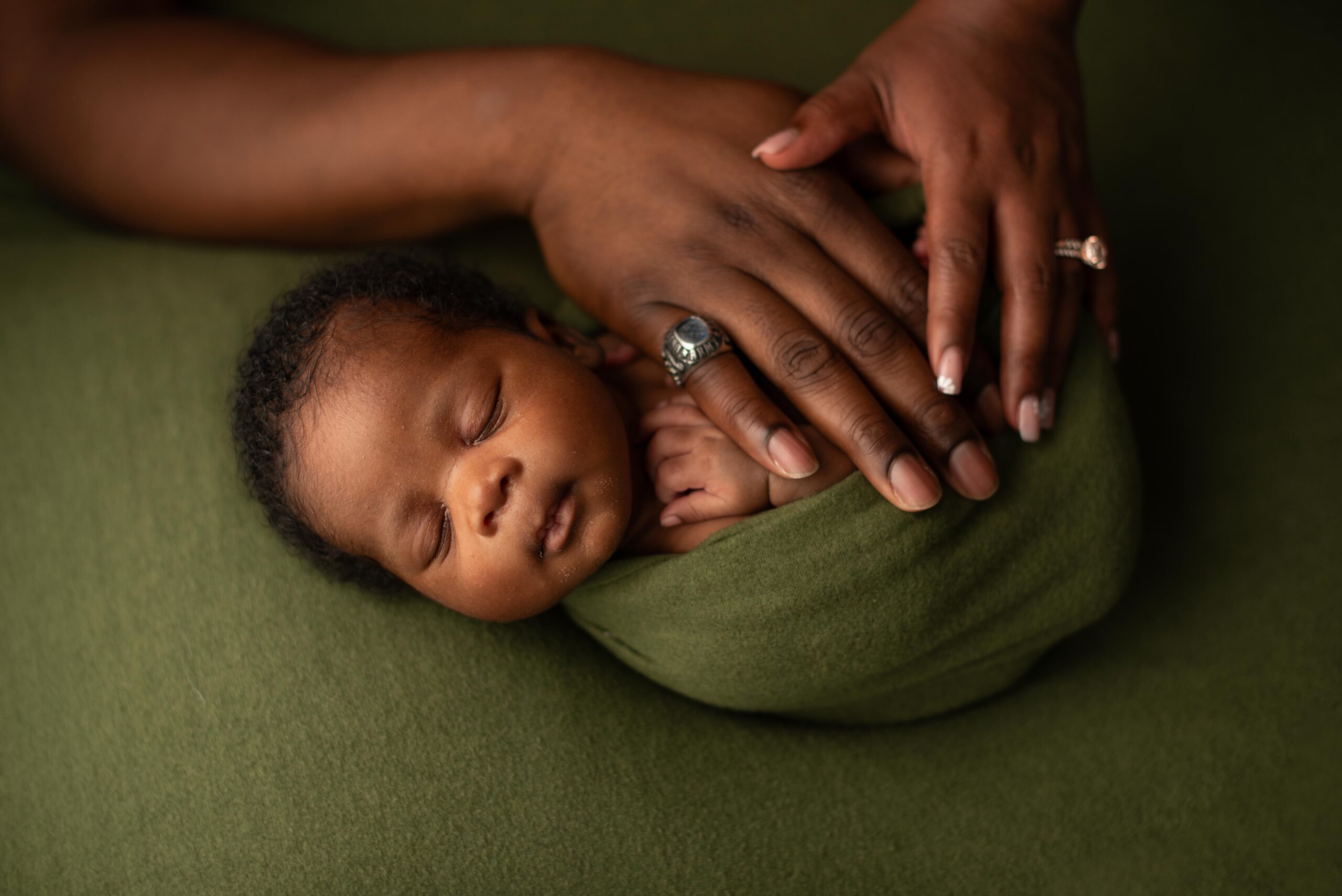 baby swaddled on table posing with parents hands on the baby
